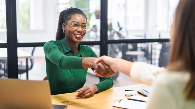 Jeune étudiante souriante serrant la main d'une collaboratrice