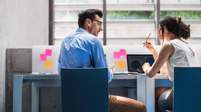 Des étudiants sont assis sur des chaises, faces à un bureau. Ils discutent et l'étudiante de droite