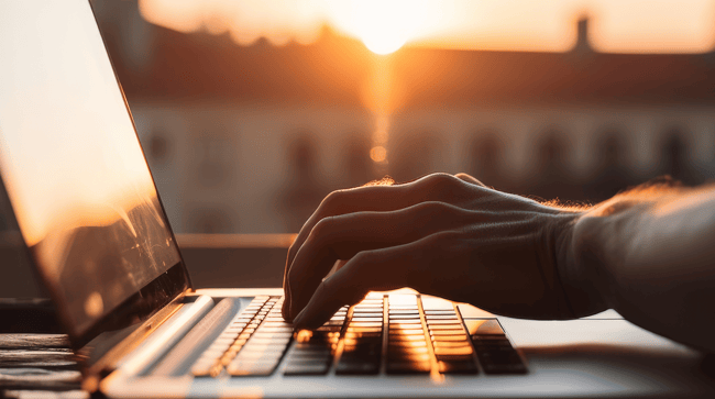 Main qui tape sur un clavier d'ordinateur avec vue sur le coucher de soleil