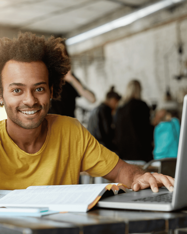 Etudiant souriant qui fait ses cours en ligne dans un café
